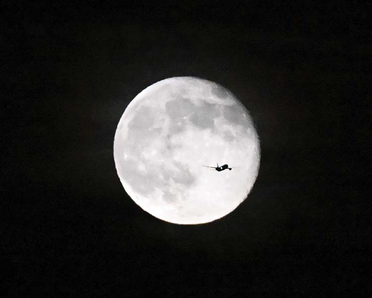A jet crosses in front of a full moon at night